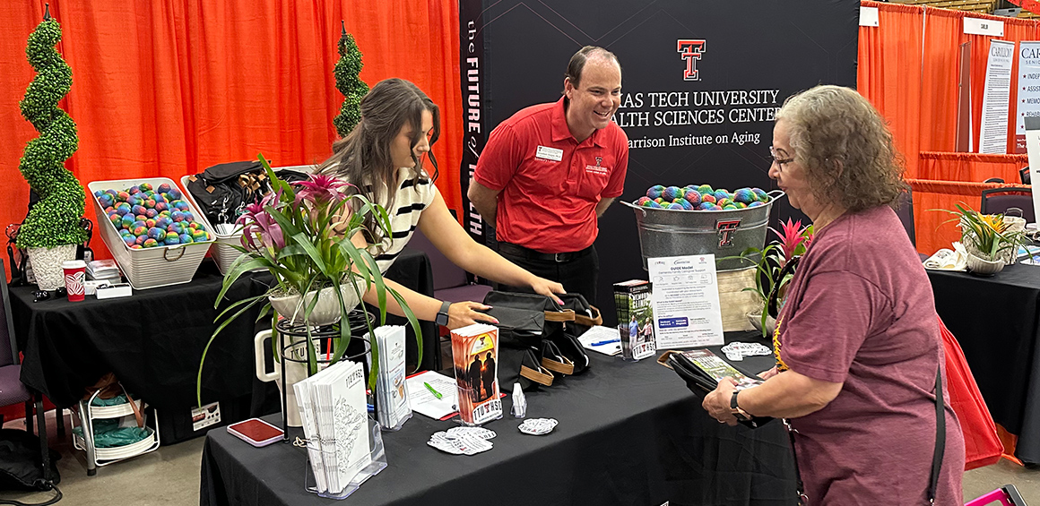Two Garrison Institute on Aging team members standing at a booth at an event engaging with an individual smiling