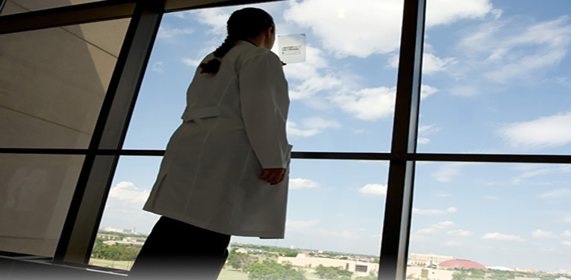 Lady in white coat standing near a window looking through a slide