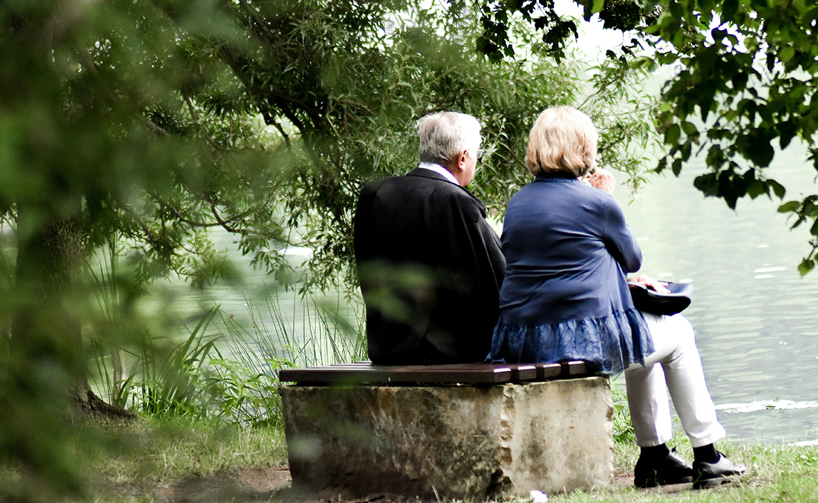 a couple sitting on a stone bench overlooking a pond surrounded by green trees