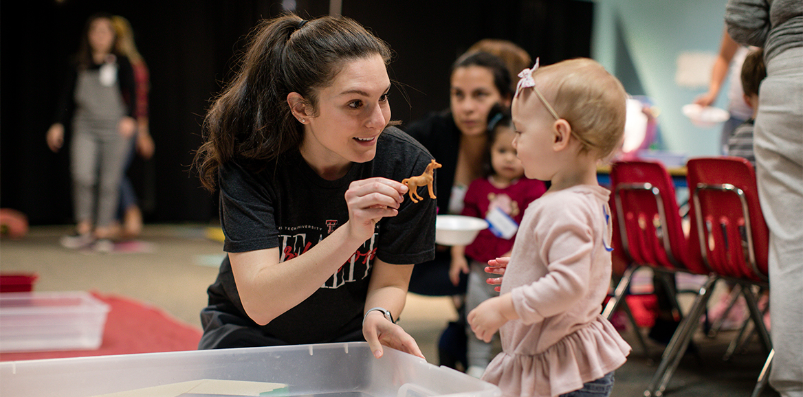 SLHS student handing a plastic toy horse to a toddler