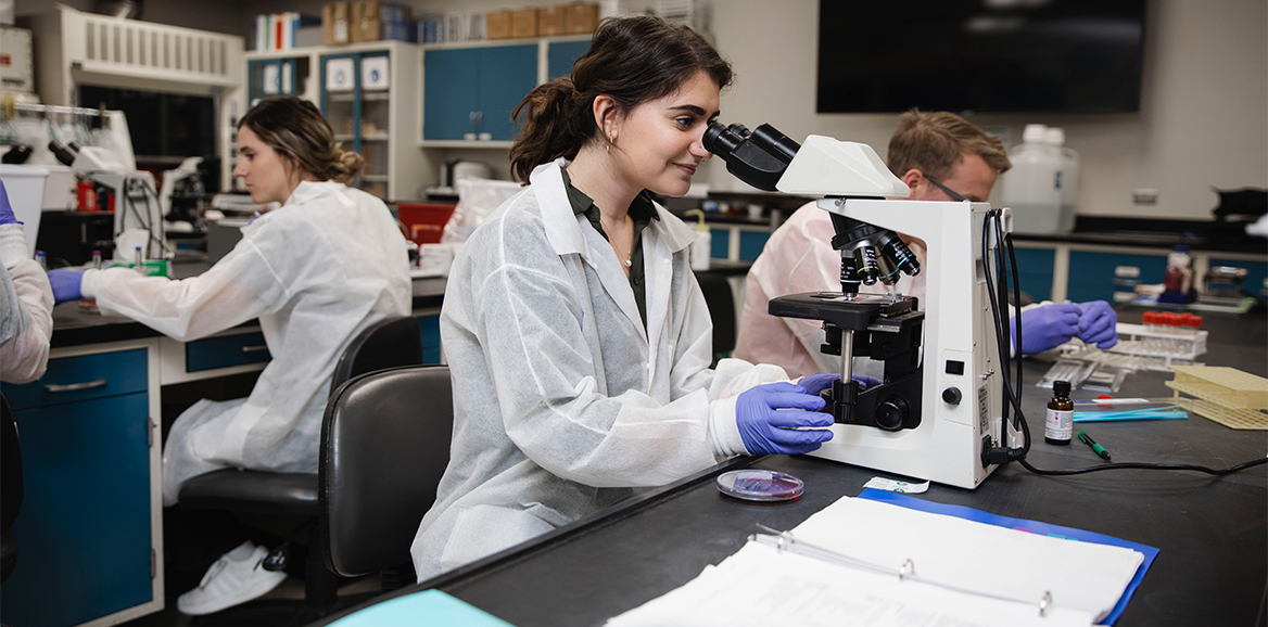 A clinical laboratory science student at TTUHSC School of Health Professions is looking into a miscroscope in the lab