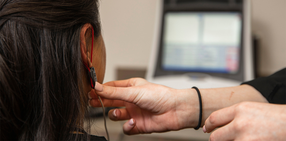 A doctor of audiology professional places a hearing device on a patient