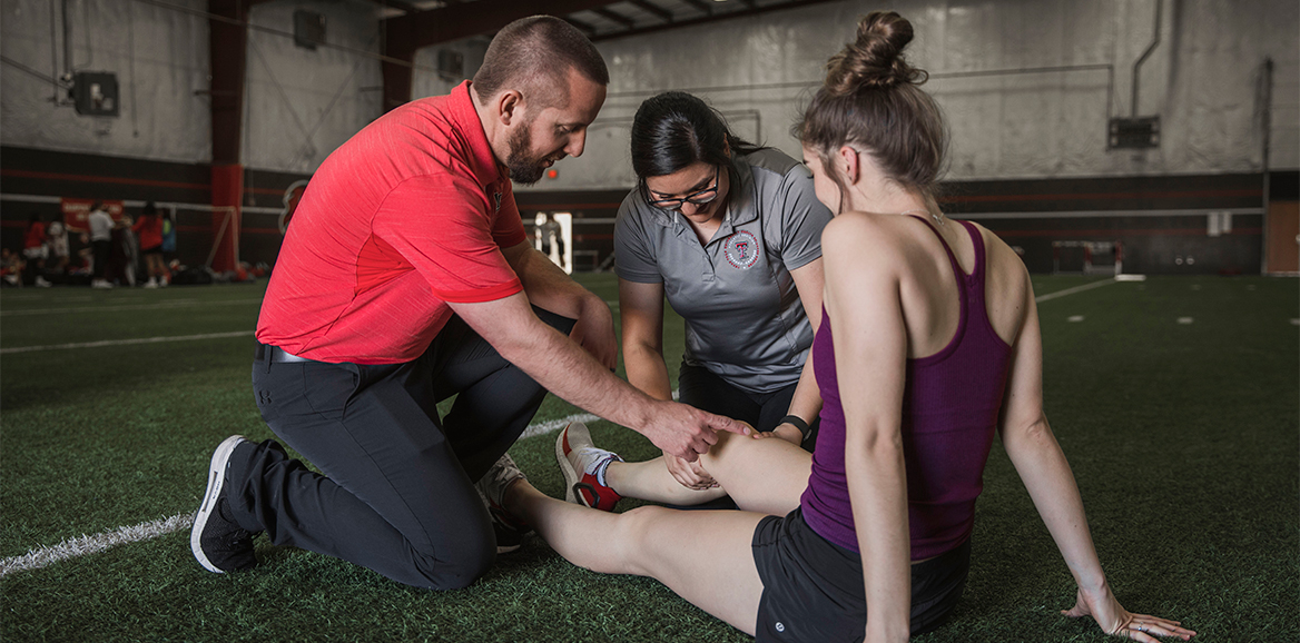 An Athletic Trainer and student checks the knee of an athlete