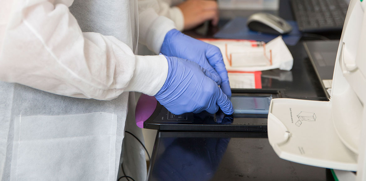 A TTUHSC molecular pathology student uses gloved hands to place a slide onto the tray of a machine in the lab