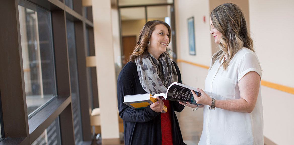 A licensed rehabilitation counselor speaks with a colleague in a hallway.