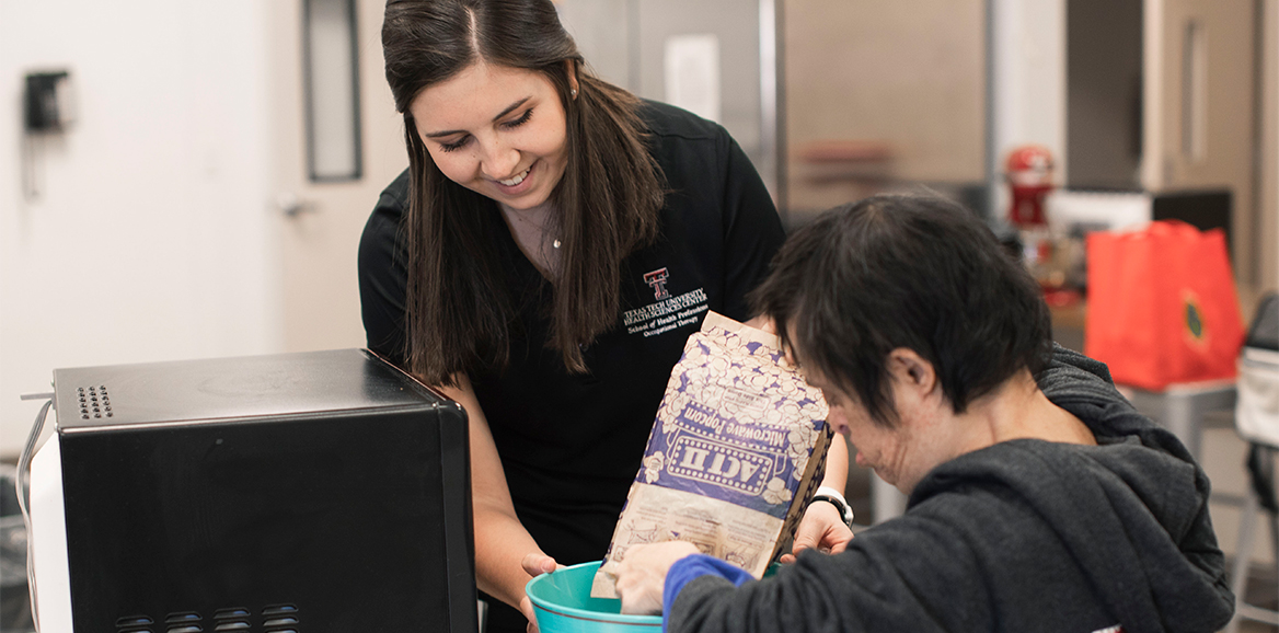A TTUHSC Occupational Therapy student helps a patient pour popcorn into a bowl