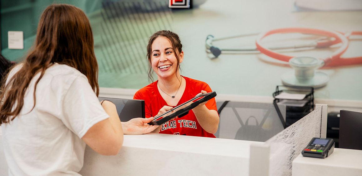 TTP volunteer smiling and handing a tablet to a patient at a checkin desk