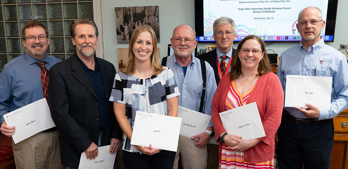 Group of School of Medicine faculty holding award envelopes standing in a classroom smiling