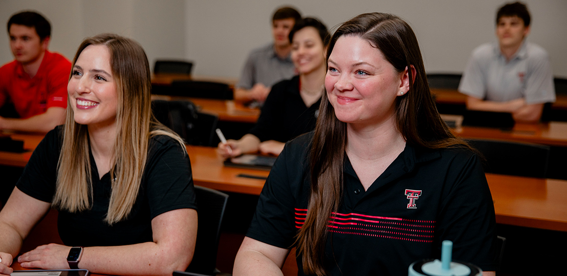Group of TTUHSC students sitting at desks in a classroom smiling looking forward
