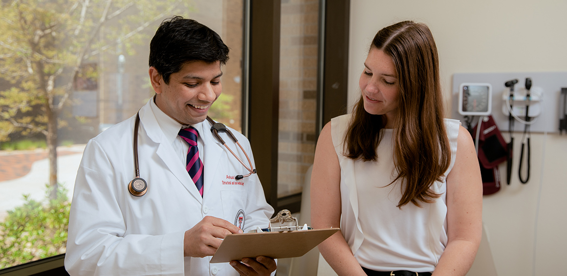 TTUHSC provider standing with a pateint in a patient room smiling in a white lab coat holding a clipboard