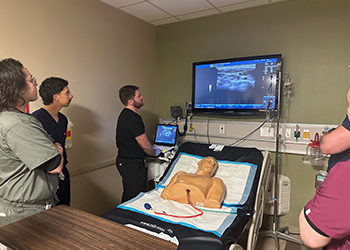 Students in a simulation room looking at a screen that is hooked up to a simulation dummy