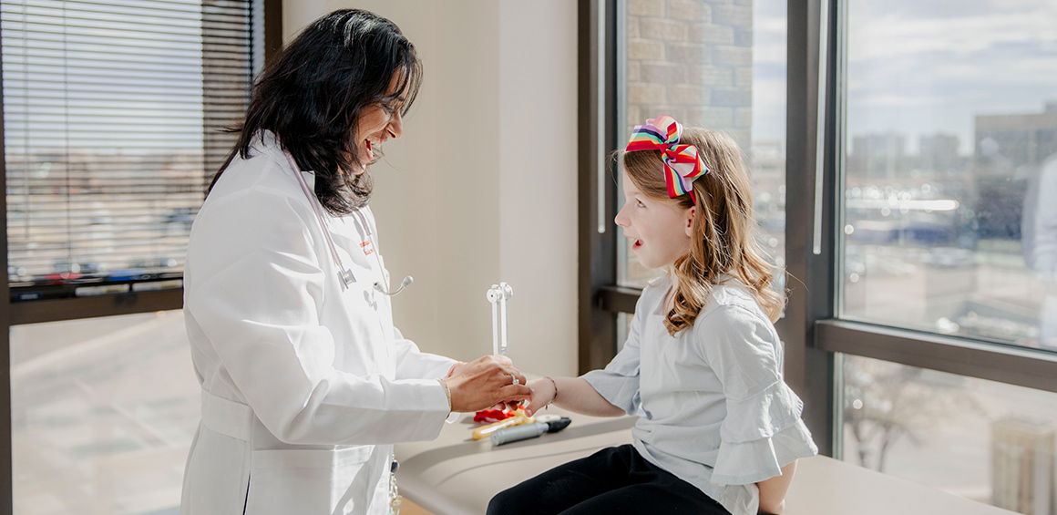 TTUHSC provider in white coat holding a female patients hand while she sits on a patient table