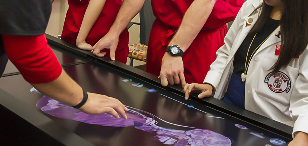 Group of students around digital tabletop displaying human anatomy