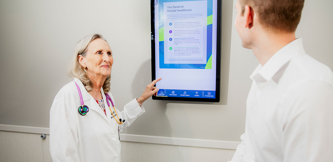 Provider in white lab coat standing at a board in a patient's room with a patient