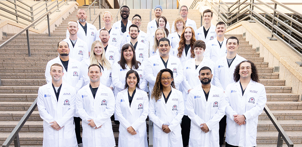 TTUHSC School of Medicine Graduate Medical Emergency Fellowship students classes of 2026 through 2028 standing on stair case infront of TTUHSC Lubbock campus in white lab coats.