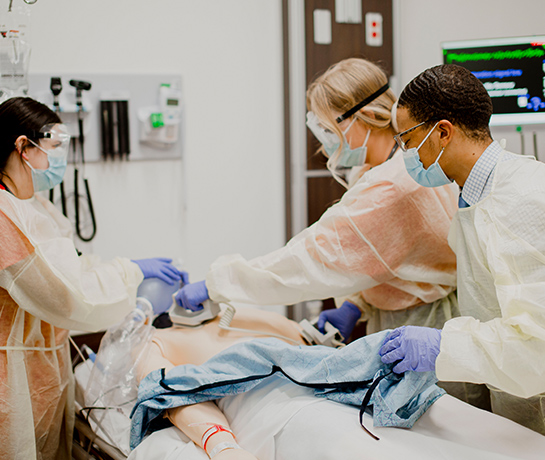 TTUHSC nursing students in PPE gear standing over SIM Center mannequin applying hands on techniques TTUHSC nursing students in PPE gear standing over SIM Center mannequin applying hands on techniques