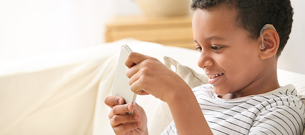 young boy playing on a cell phone and wearing a hearing aid