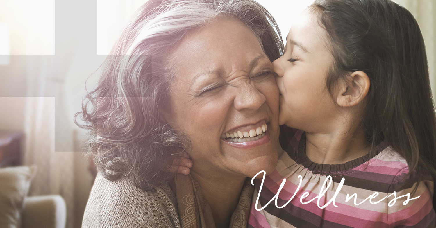 hispanic grandmother, smiling and laughing, while her grandaughter kisses her