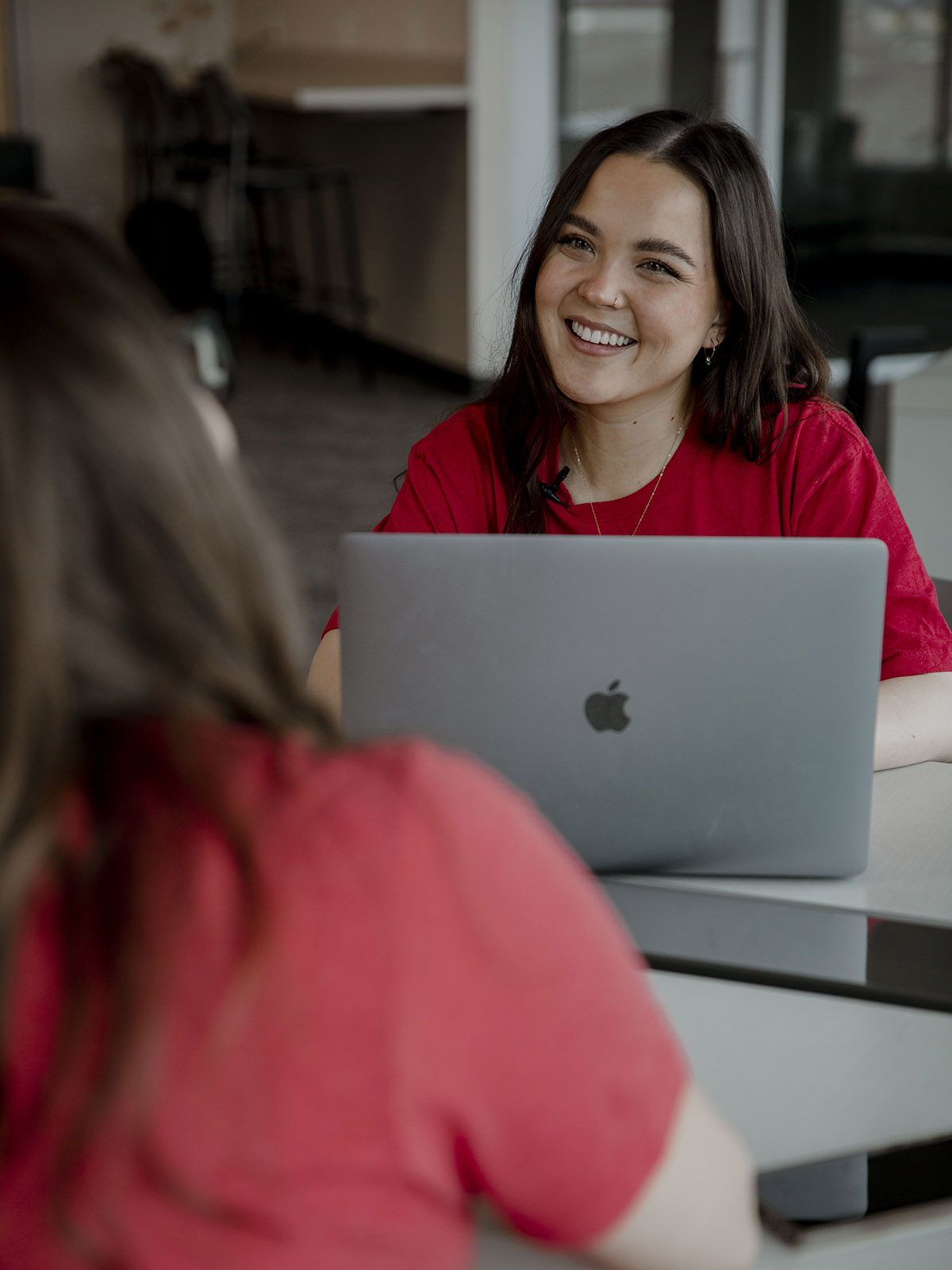 TTUHSC Dallas/Mansfield student smiling at another student with laptop at a table.
