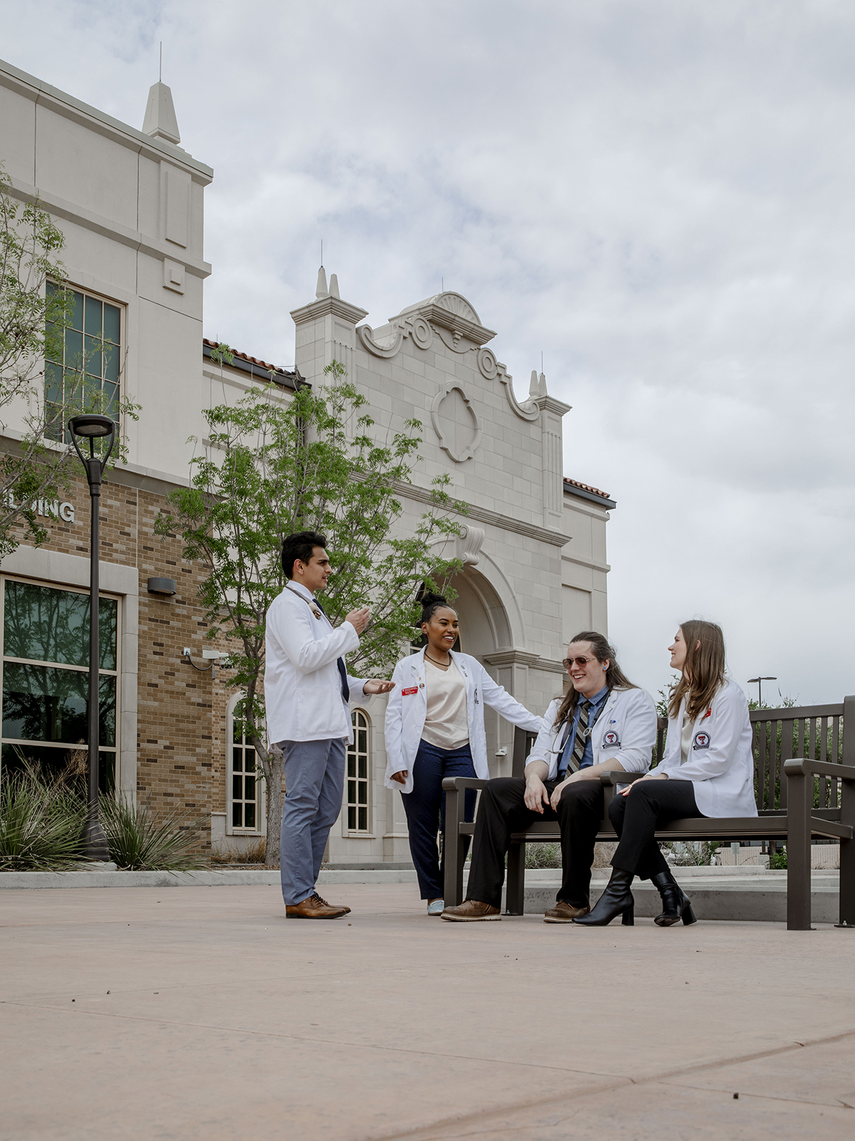 TTUHSC Odessa medical students standing and sitting together outside on a bench with the building in the background