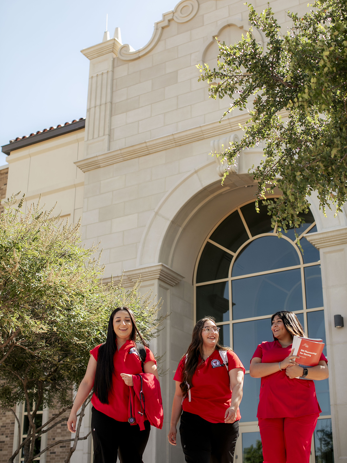 TTUHSC Odessa nursing students walking together outside wearing red scrubs and holding books, bags, and backpacks