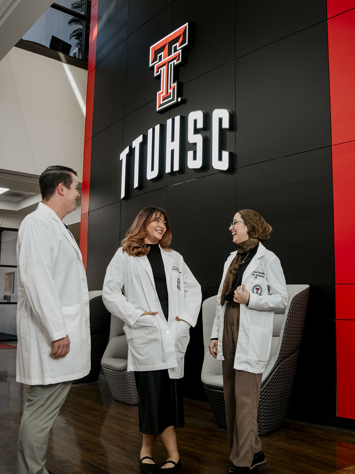 TTUHSC Lubbock Psychiatry students and faculty standing together in white coats in front of a wall sign with the Double T logo