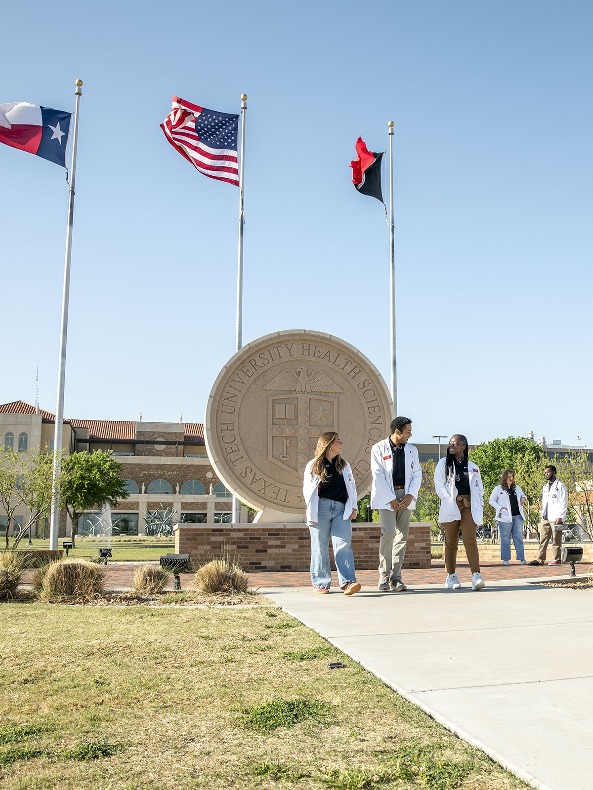 TTUHSC Lubbock students walking outside together in front of the flags and seal.