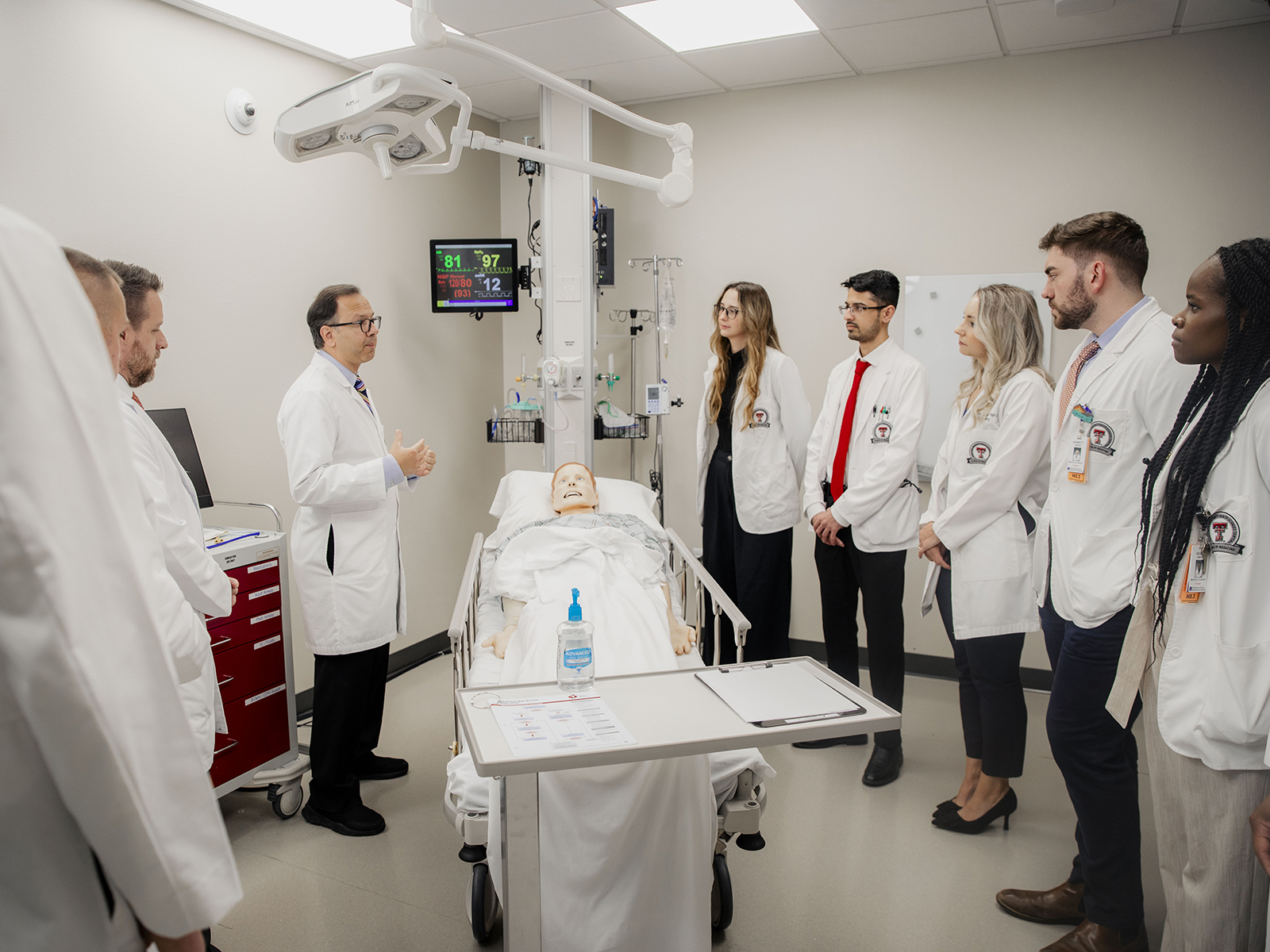 TTUHSC Amarillo Surgery Residents standing around mannequin in simulation room listening to professor speak.