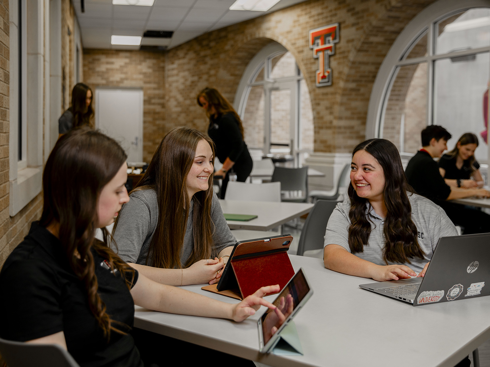 TTUHSC Amarillo students sitting at a table together smiling looking at screens and each other.