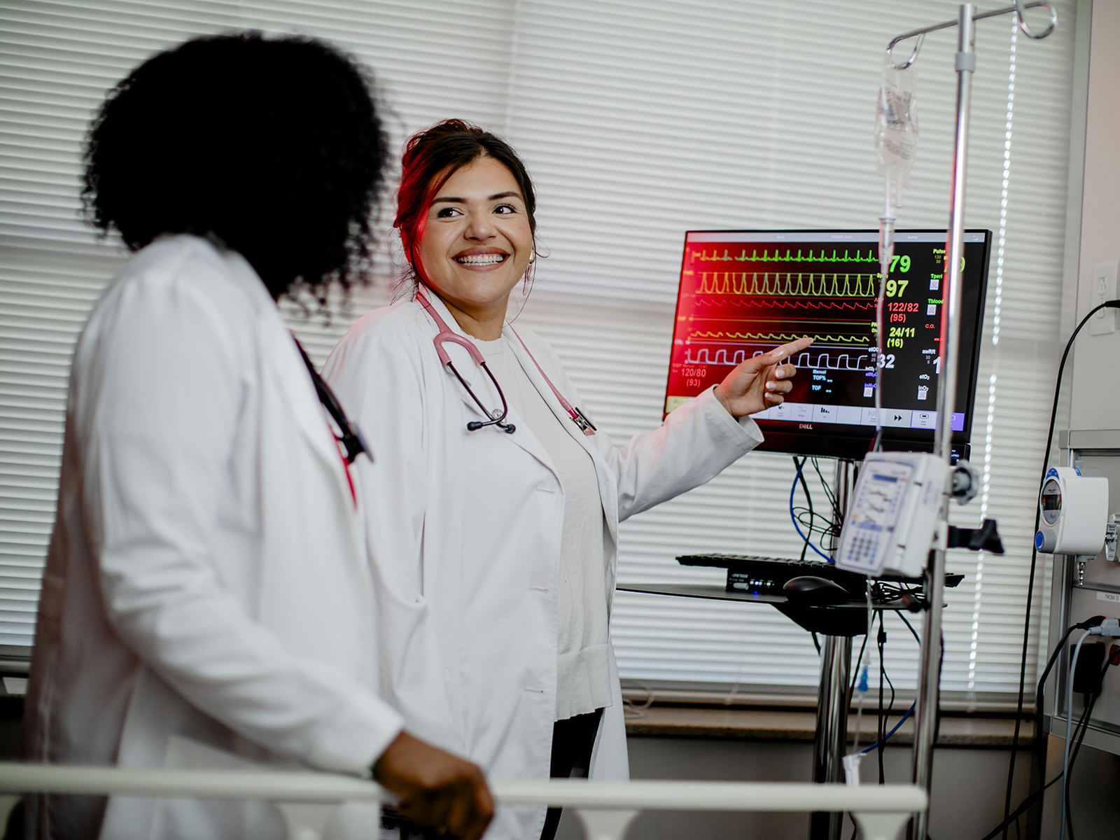 TTUHSC Odessa students stand in white coats with stethoscopes looking at screen showing heartbeat vitals