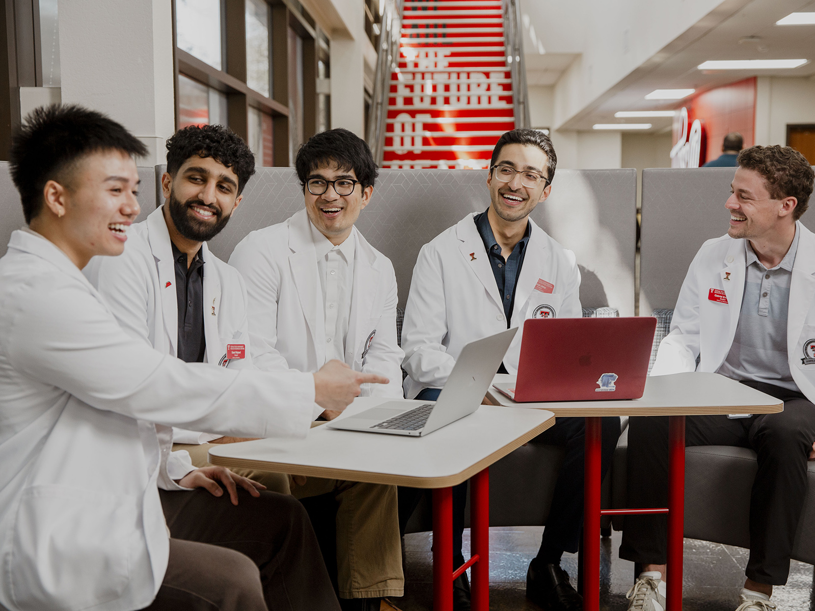 TTUHSC Lubbock students in white coats sitting together at a table in the Academic Classroom Building lobby