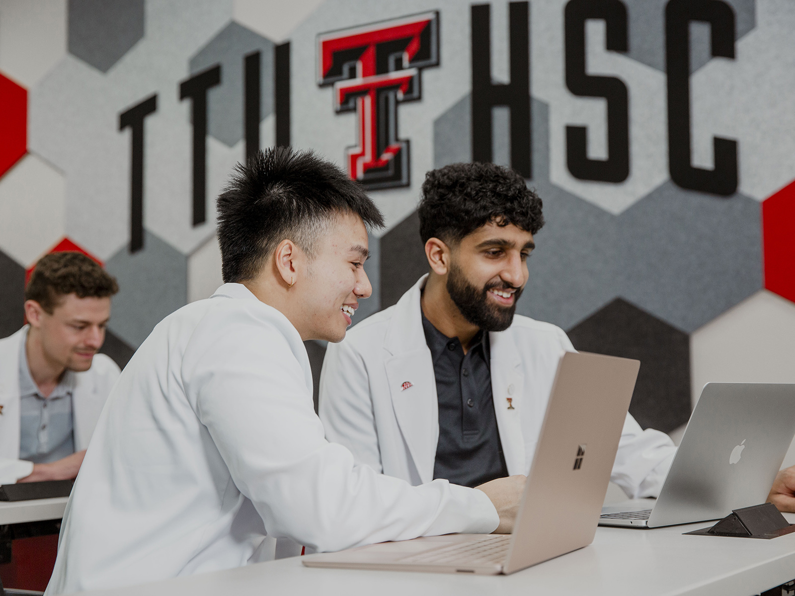 TTUHSC students sitting in a classroom together with the wall logo displayed in the background.