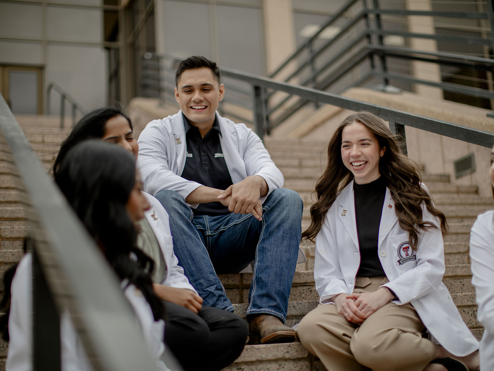 TTUHSC Lubbock students sitting on the steps of the building entrance talking.