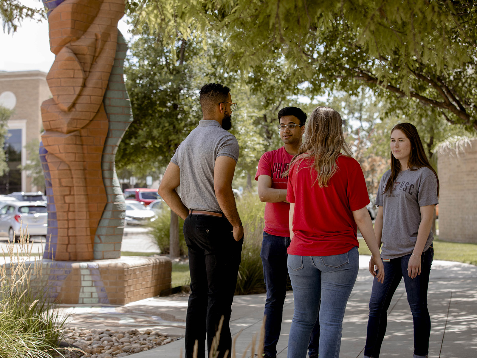 TTUHSC Amarillo students gathered together in the shade outside talking near a public art statue in the background.