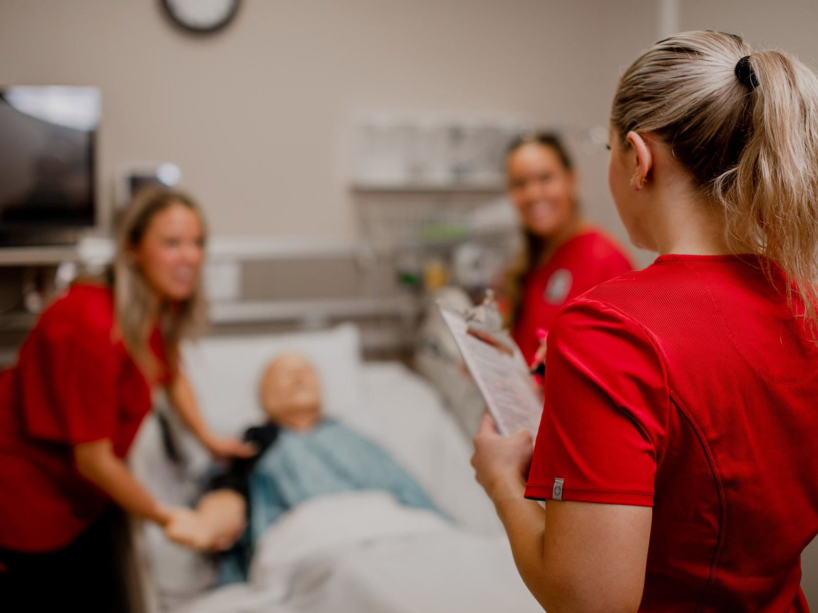 TTUHSC Abilene nursing students with a clipboard and simulation mannequin sitting in a hospital bed.