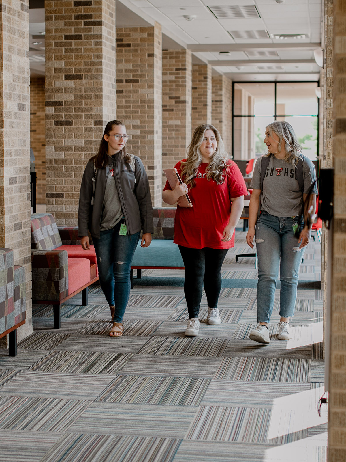 Three students at TTUHSC Abilene walking together carrying a laptop and wearing backpacks.