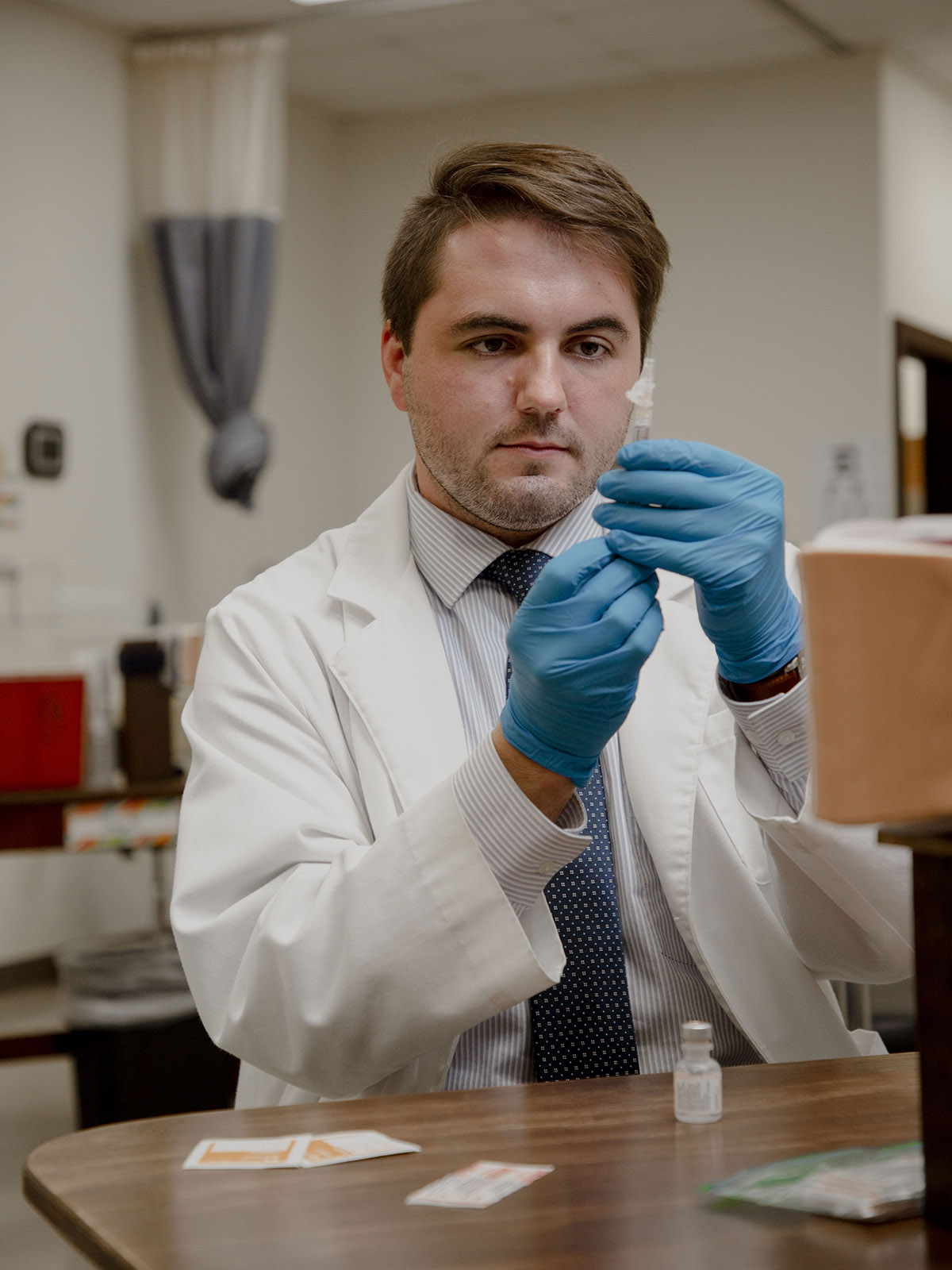 Person wearing globes, lab coat, preparing a syringe needle injection and medicine sitting at a table .