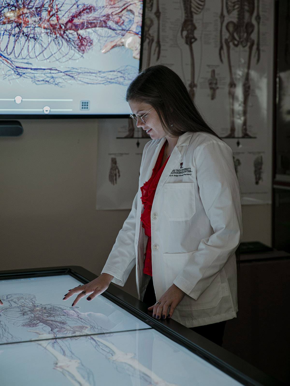 Student wearing glasses touching a flat screen simulation image of body systems.