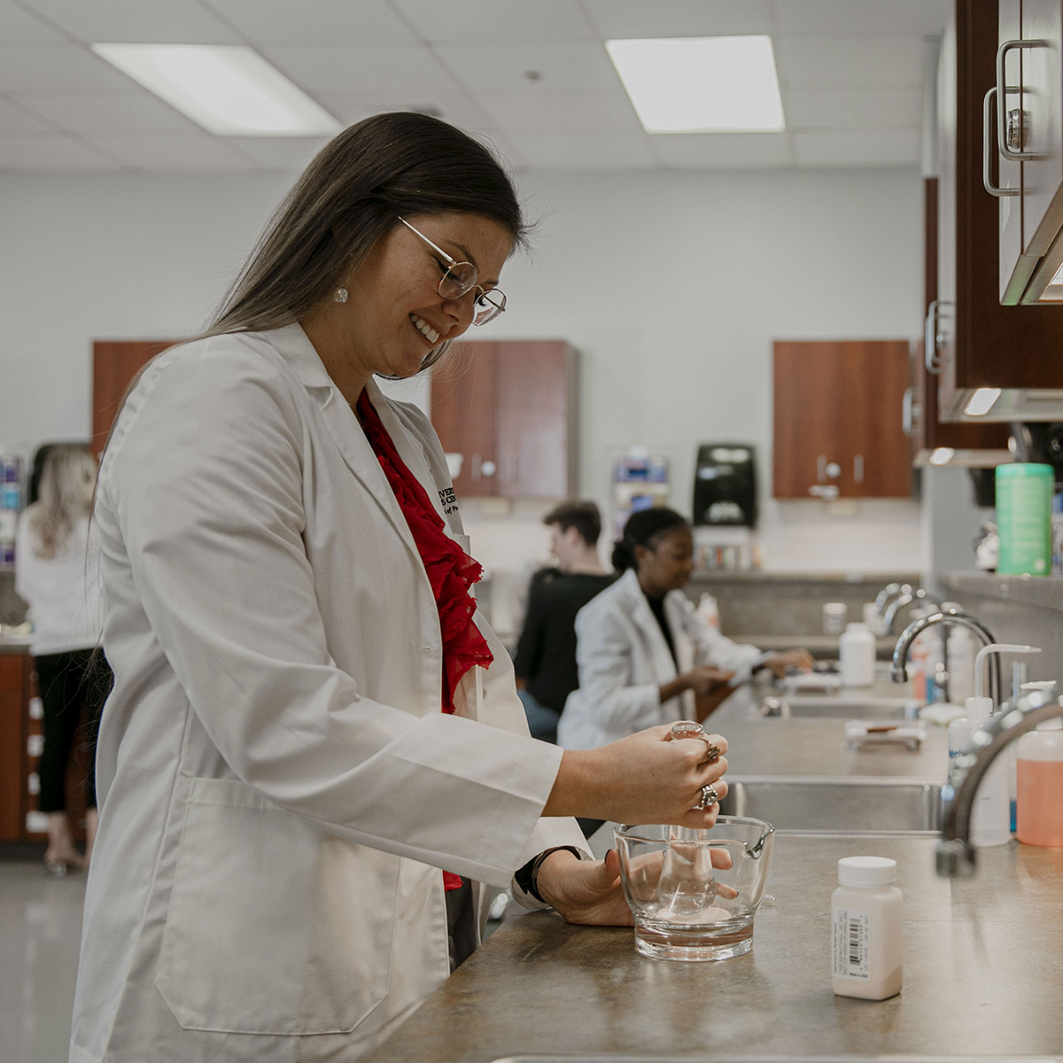 TTUHSC Abilene Pharmacy student smiling wearing glasses with a mortar and pestle blending substance from a container.