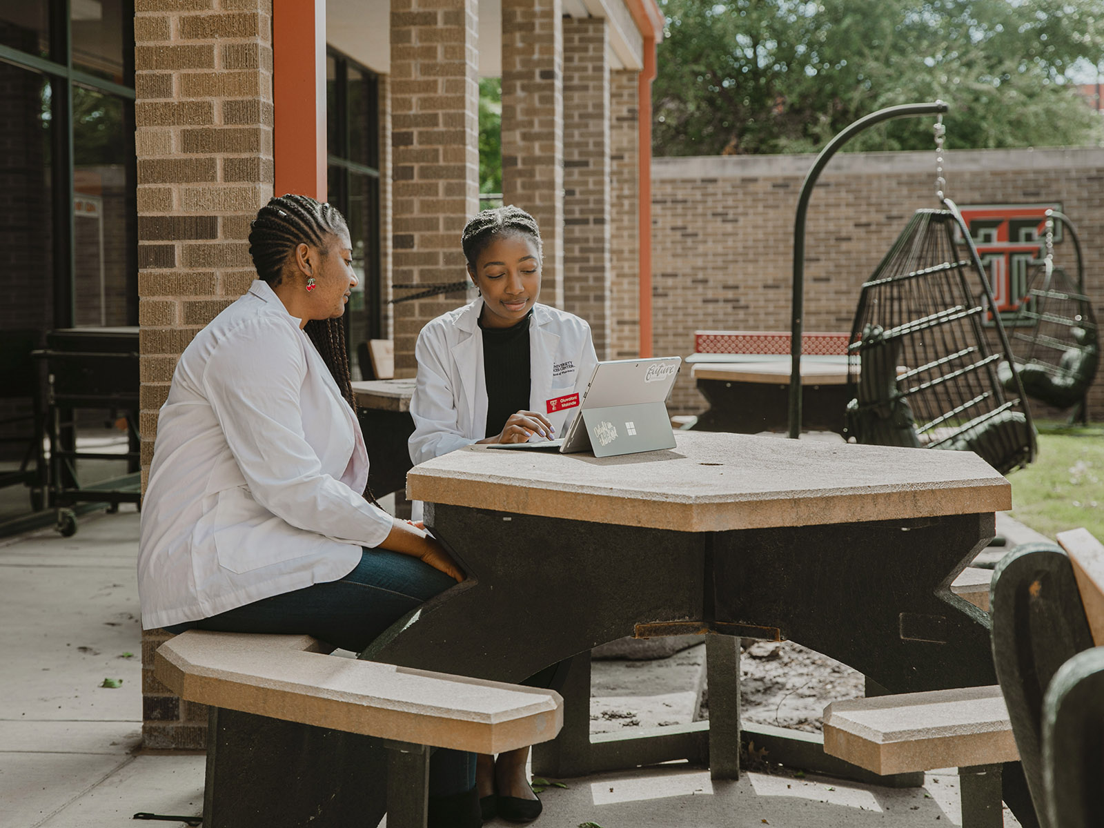 Two students at TTUHSC Abilene sitting together at a picnic table looking at an ipad.