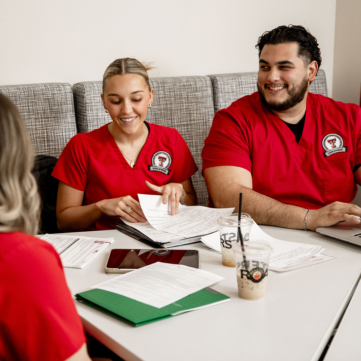 TTUHSC Amarillo nursing students wearing red scrubs drinking coffee with books, papers and study materials on the table.