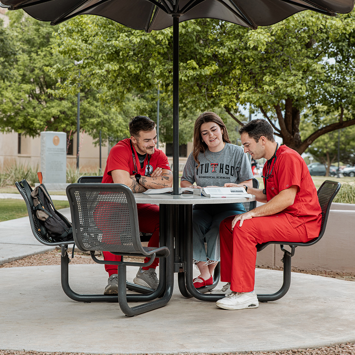 TTUHSC Lubbock students sitting together at a picnic table outside with trees in the background