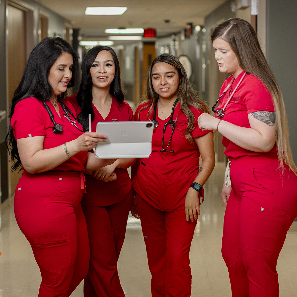 TTUHSC Odessa nursing students standing together in a hallway looking at the same screen.