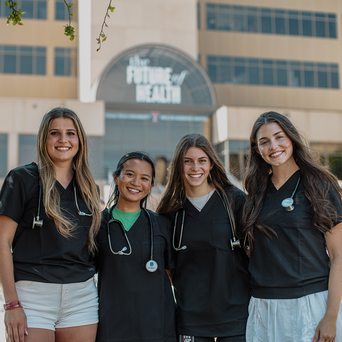 TTUHSC Lubbock students standing side by side with matching shirts and stethoscopes around their necks with the building in the background.