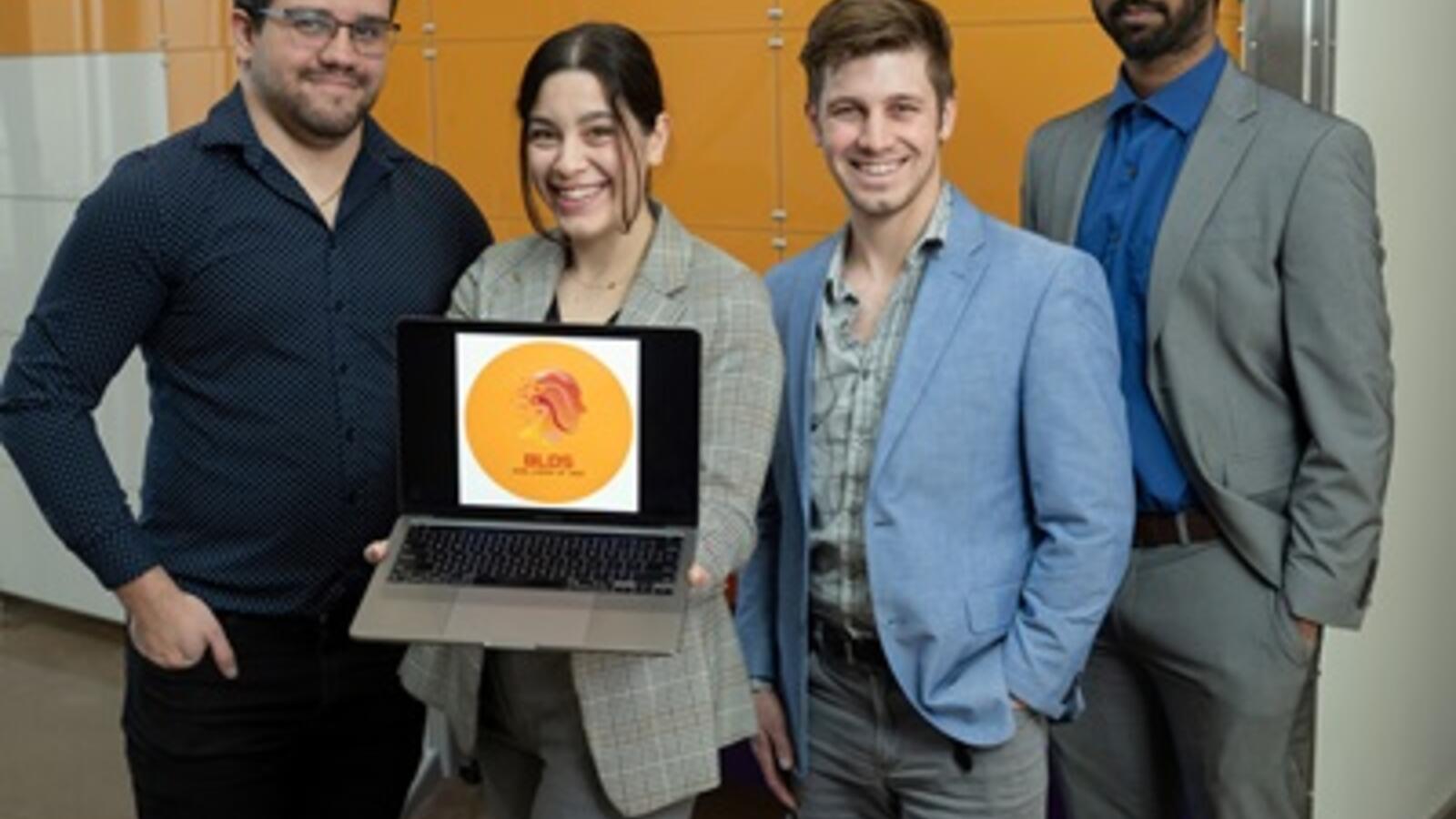 group of four people facing the camera and posing with a laptop