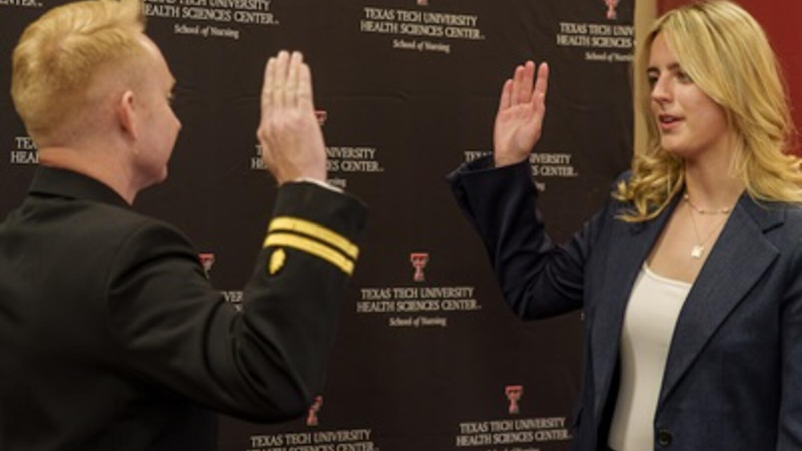 woman raising her hand to get sworn into the military by a man whose hand is also raised