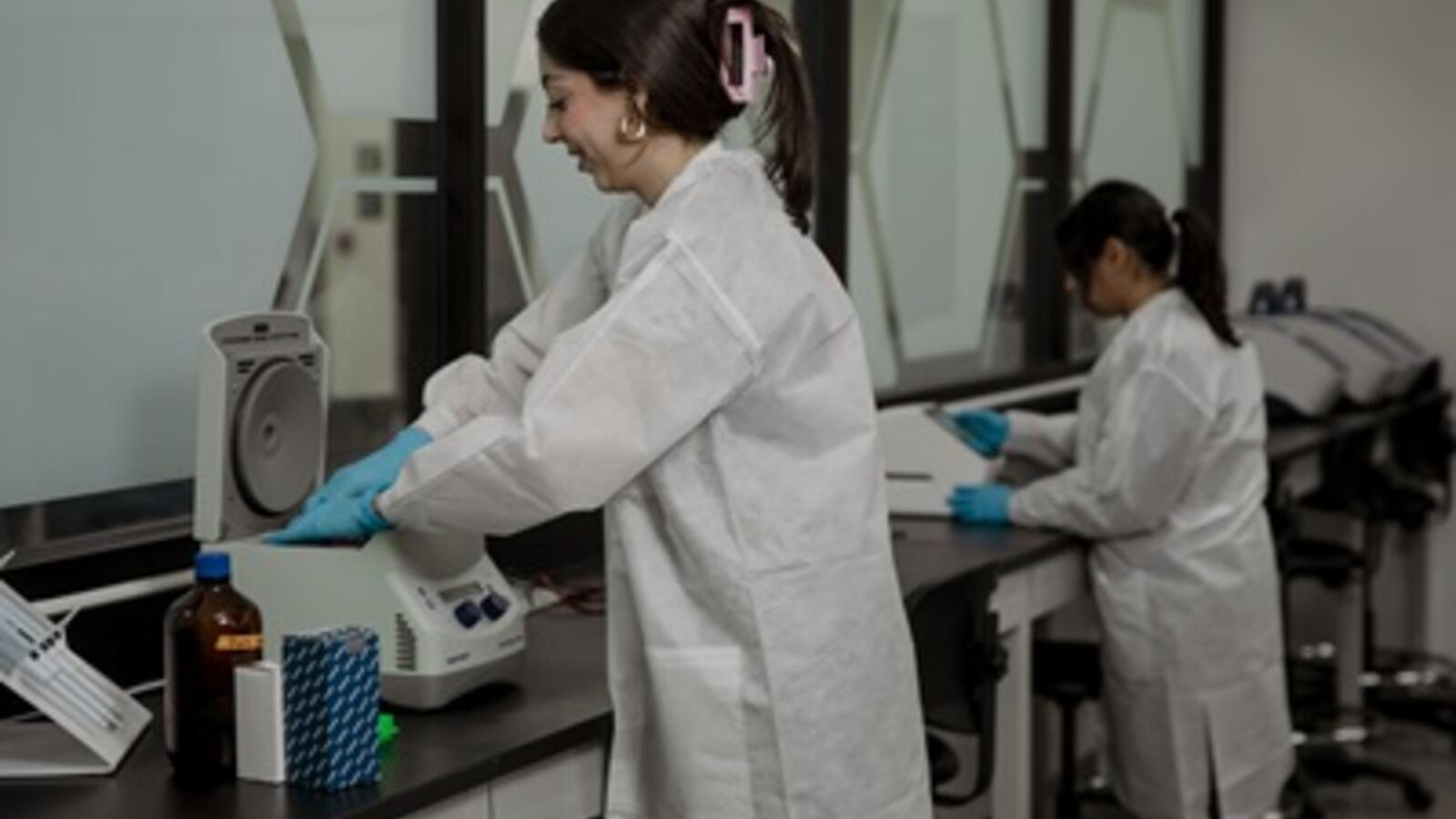 woman working with DNA lab equipment, wearing scrubs and gloves
