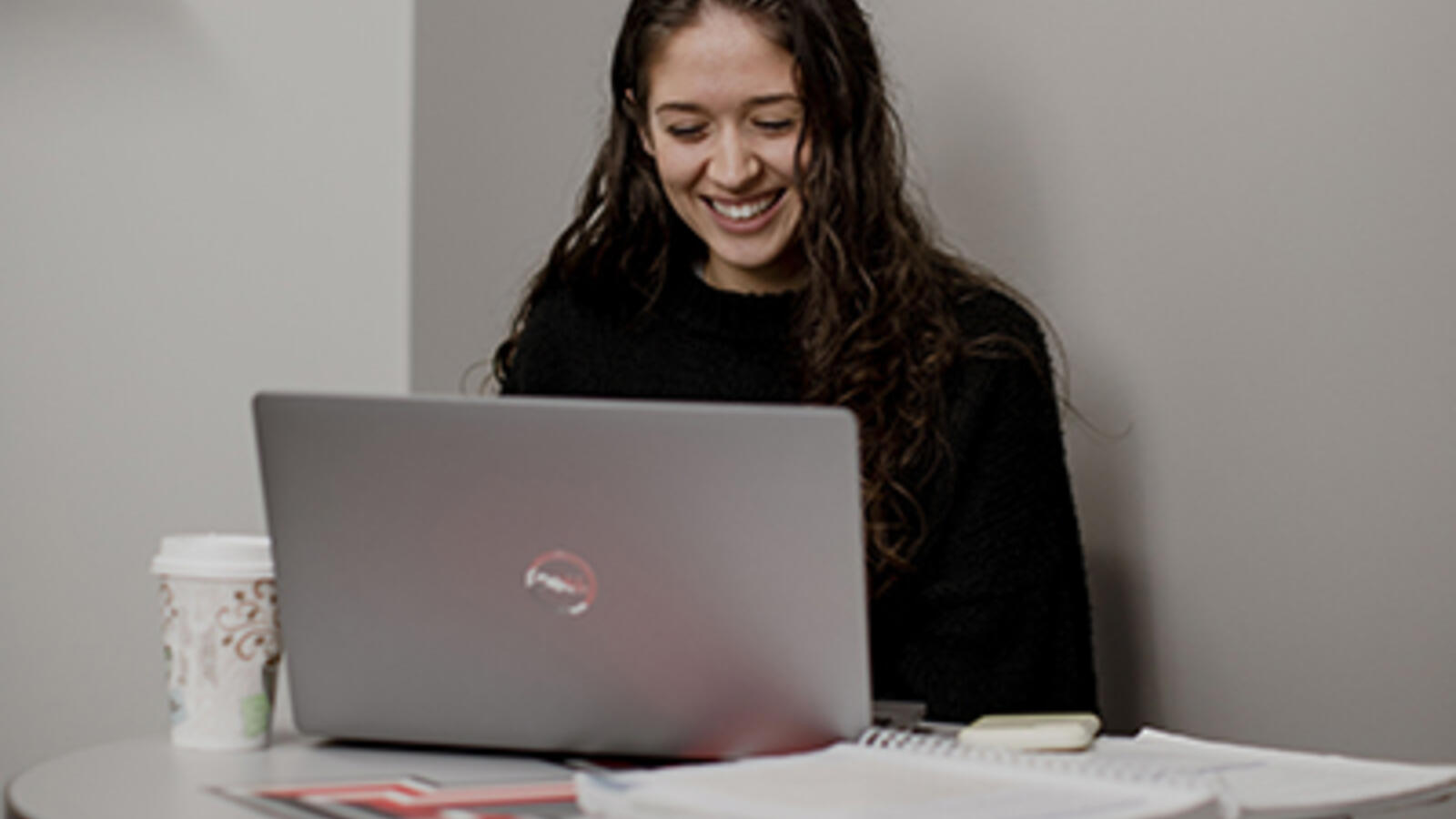 woman smiling at her laptop with coffee