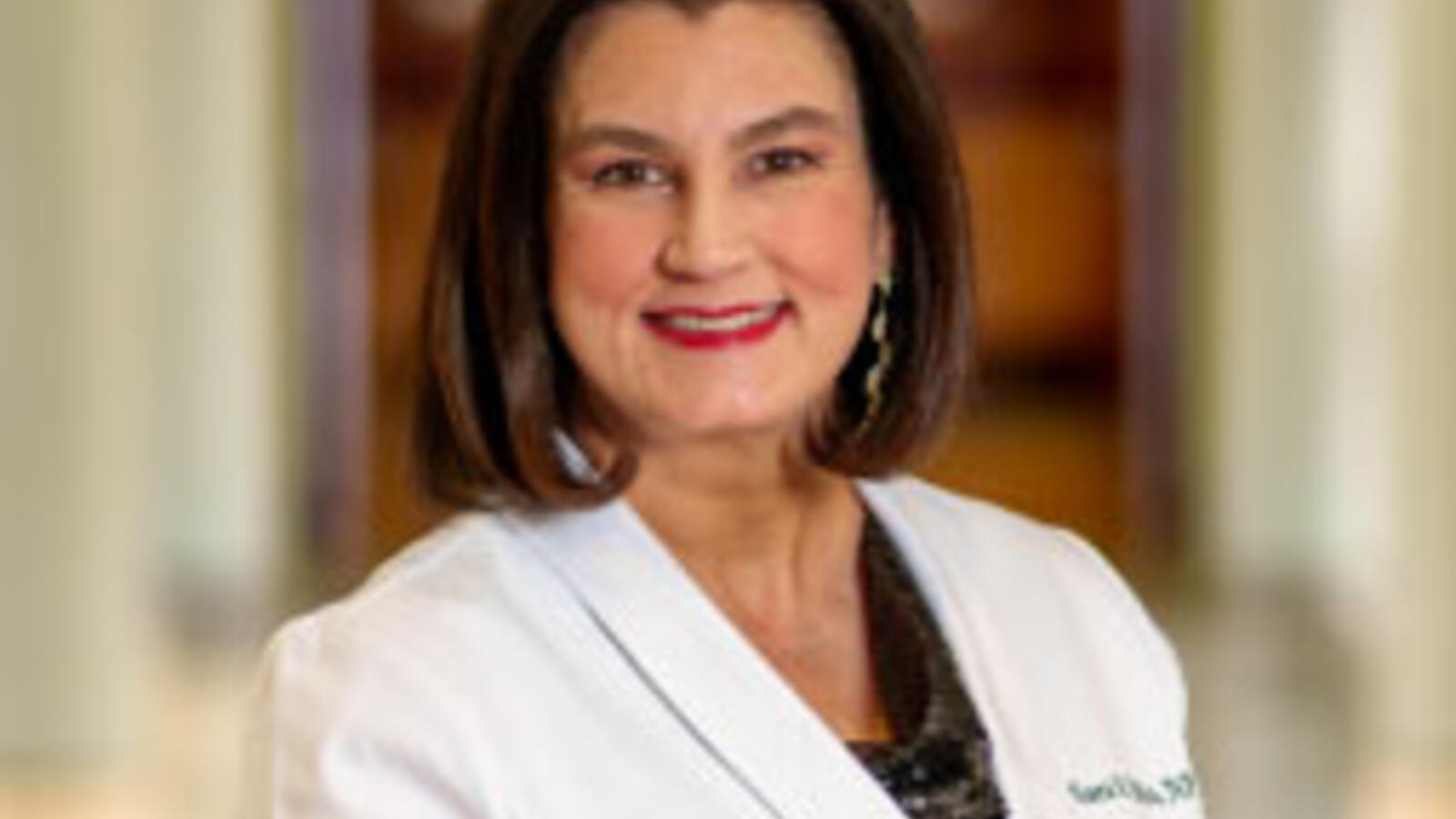 Woman nurse practitioner wears a white coat and stands in a hallway.