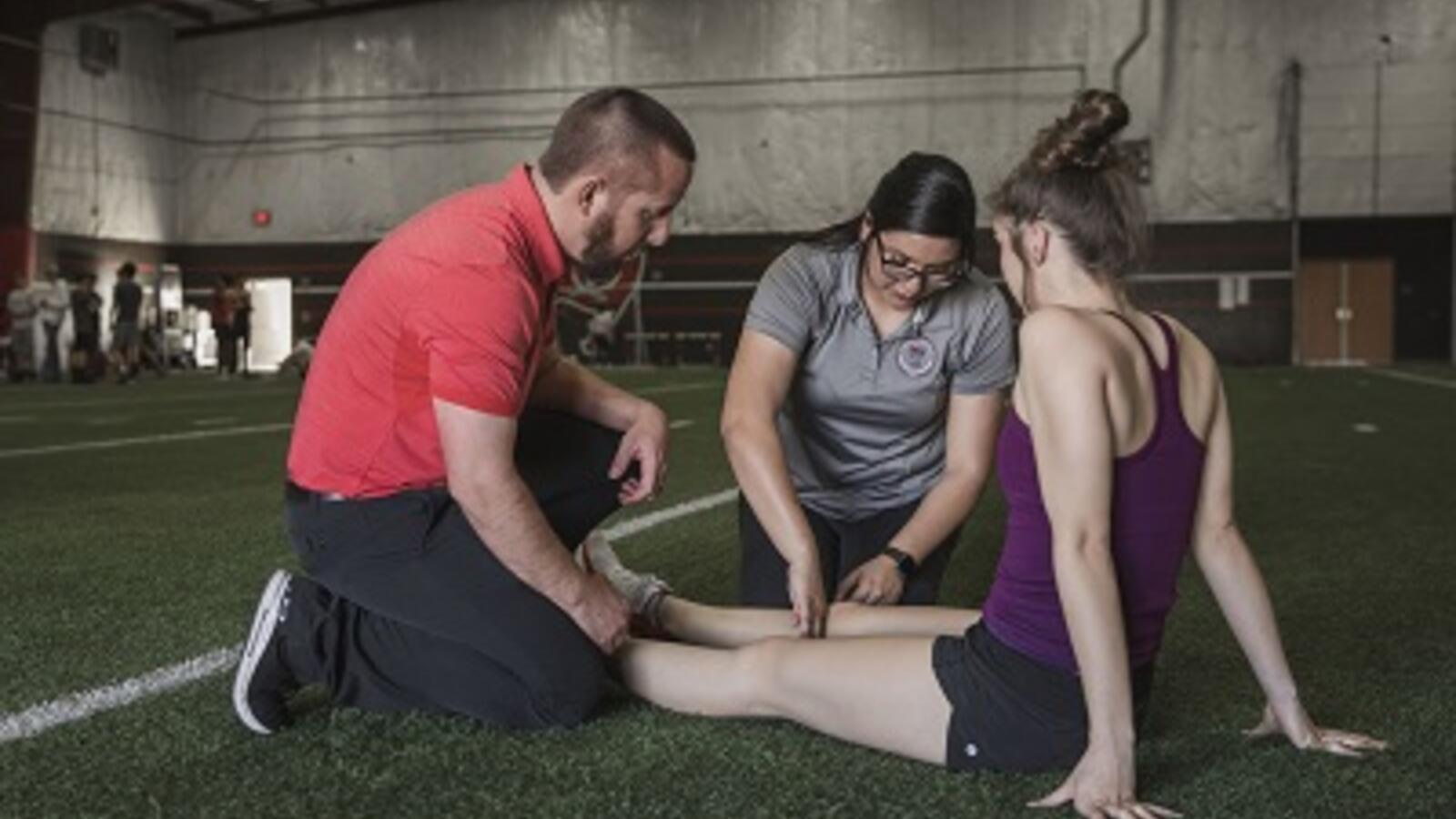 physical therapist and student athlete sitting on a field